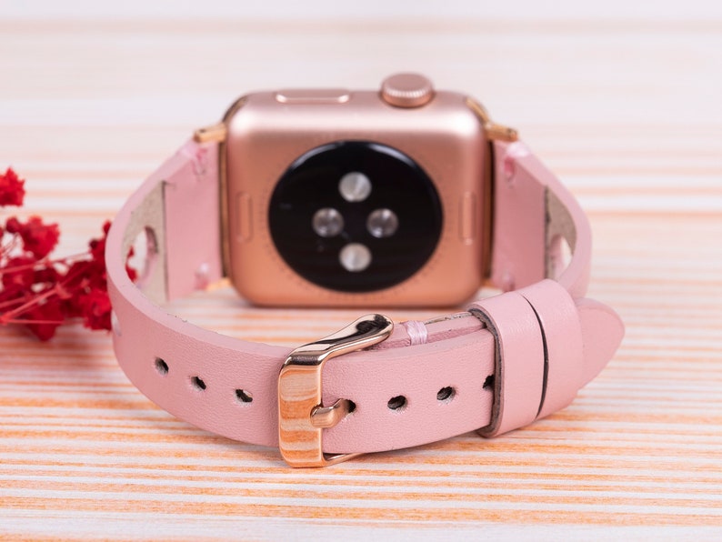 Peut inclure: Un bracelet de montre en cuir rose avec une boucle en or rose et une Apple Watch en or rose.