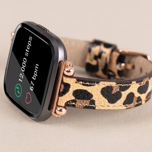 Puede incluir: Un rastreador de fitness negro con una banda de estampado de leopardo. La pantalla muestra "12.000 pasos" y "67 ppm".