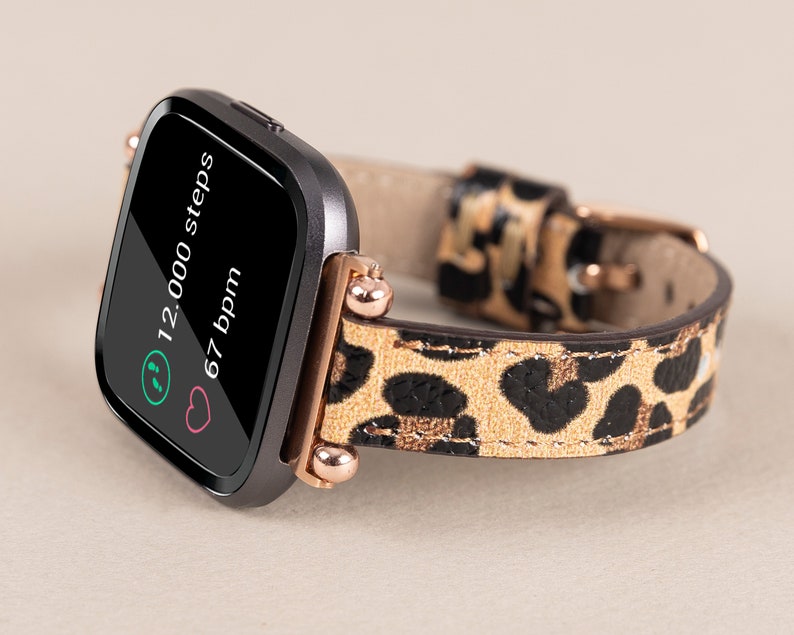 Puede incluir: Un rastreador de fitness negro con una banda de estampado de leopardo. La pantalla muestra "12.000 pasos" y "67 ppm".