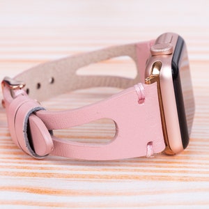 Peut inclure: Un bracelet de montre en cuir rose avec une Apple Watch en or rose.
