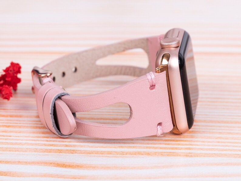 Peut inclure: Un bracelet de montre en cuir rose avec une Apple Watch en or rose.