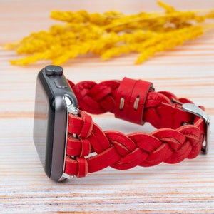 Puede incluir: Una correa de reloj de cuero trenzado roja con una hebilla plateada. La correa est&aacute; dise&ntilde;ada para un Apple Watch.