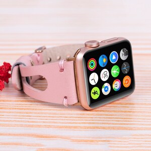 Peut inclure: Une Apple Watch en or rose avec un bracelet en cuir rose. Le cadran de la montre affiche une vari&eacute;t&eacute; d'ic&ocirc;nes d'applications, notamment une horloge, une boussole et un moniteur de fr&eacute;quence cardiaque.