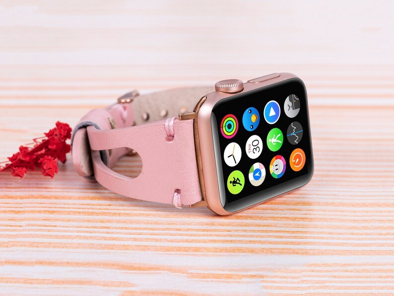 Peut inclure: Une Apple Watch en or rose avec un bracelet en cuir rose. Le cadran de la montre affiche une vari&eacute;t&eacute; d'ic&ocirc;nes d'applications, notamment une horloge, une boussole et un moniteur de fr&eacute;quence cardiaque.