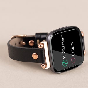 May include: Black leather fitness tracker with a rose gold band and a black screen displaying 12,000 steps and 67 bpm.