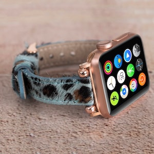 May include: A rose gold Apple Watch with a blue and brown leopard print leather band. The watch face displays the time, date, and various app icons.