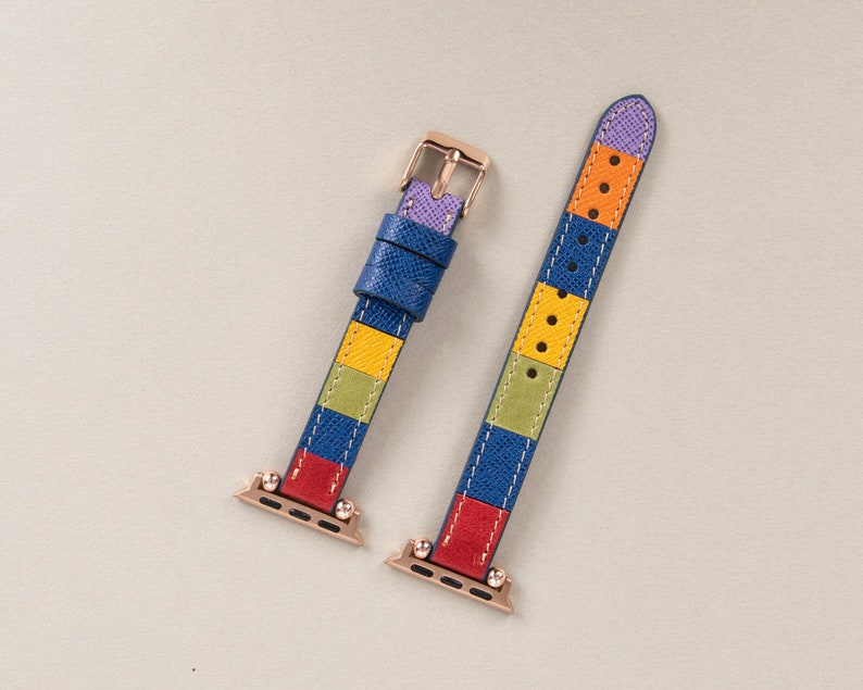 K&ouml;nnte beinhalten: Ein farbenfrohes Armband mit einem gestreiften Muster in Blau, Gelb, Gr&uuml;n, Rot und Lila. Das Armband ist aus Leder und hat eine ros&eacute;goldene Schlie&szlig;e.