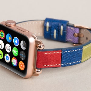 K&ouml;nnte beinhalten: Eine ros&eacute;goldene Apple Watch mit einem mehrfarbigen Lederarmband. Das Armband besteht aus rotem, blauem, gr&uuml;nem und violettem Leder. Das Zifferblatt der Uhr zeigt die Zeit, das Datum und mehrere App-Symbole.