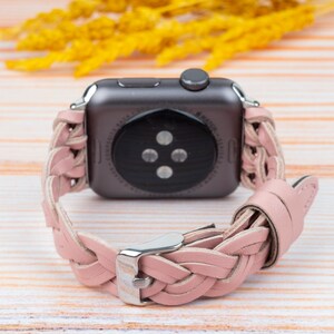 K&ouml;nnte beinhalten: Ein rosafarbenes geflochtenes Lederarmband f&uuml;r eine Apple Watch. Das Armband ist auf der R&uuml;ckseite der Uhr zu sehen, wobei das Zifferblatt von der Kamera abgewandt ist.