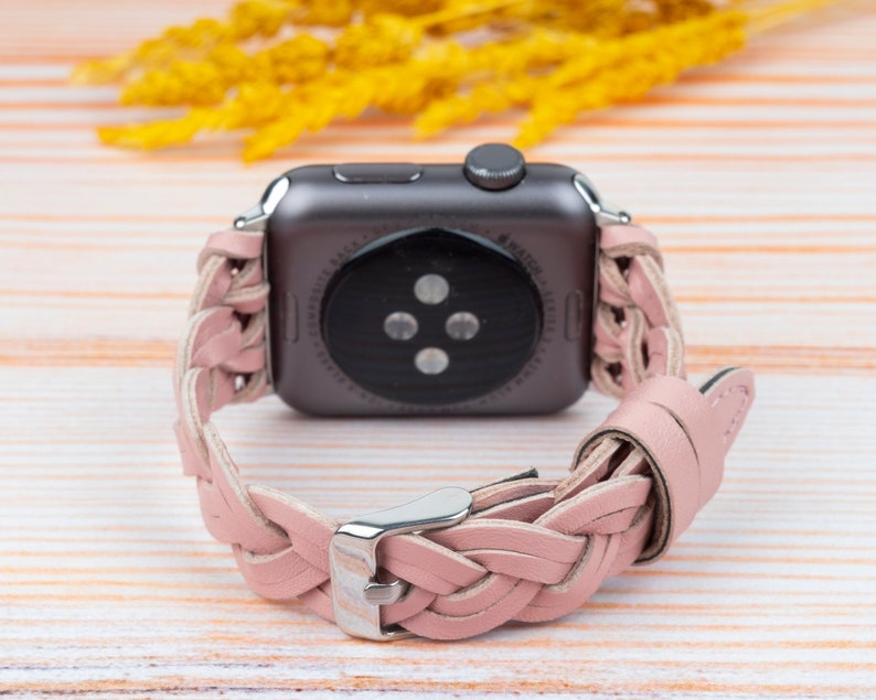 K&ouml;nnte beinhalten: Ein rosafarbenes geflochtenes Lederarmband f&uuml;r eine Apple Watch. Das Armband ist auf der R&uuml;ckseite der Uhr zu sehen, wobei das Zifferblatt von der Kamera abgewandt ist.