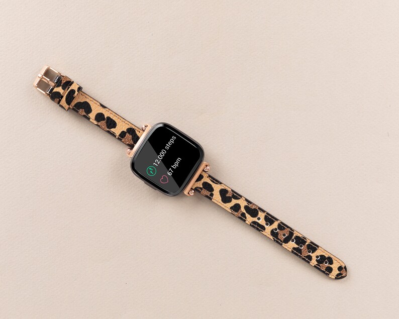 Puede incluir: Un rastreador de fitness negro con una banda de estampado de leopardo. La pantalla muestra "12.000 pasos" y "67 ppm".