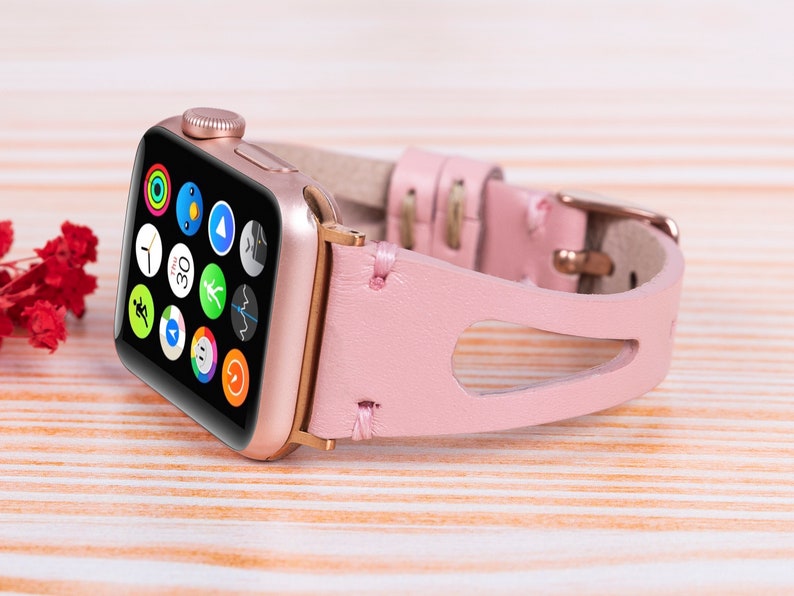 Peut inclure: Un bracelet de montre en cuir rose avec une Apple Watch dor&eacute;e. Le cadran de la montre affiche une vari&eacute;t&eacute; d'applications, y compris une minuterie r&eacute;gl&eacute;e sur 30 secondes.