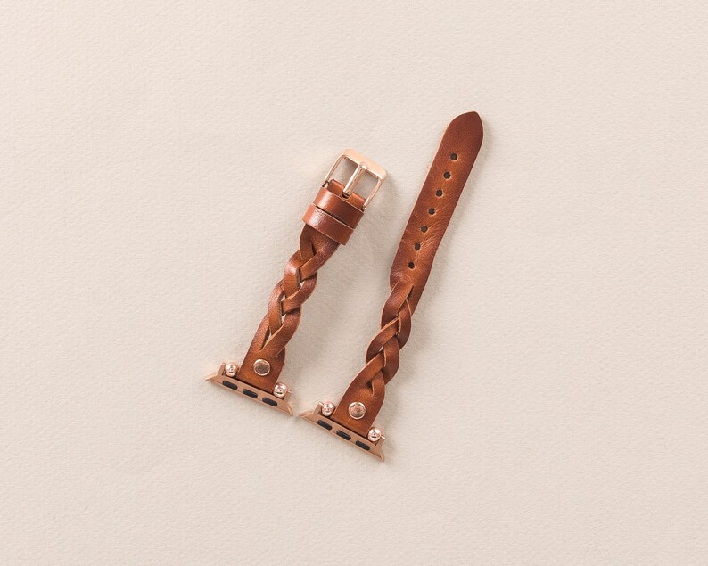 Puede incluir: Dos correas de reloj trenzadas de cuero marr&oacute;n con herrajes dorados. Las correas est&aacute;n dise&ntilde;adas para Apple Watches.