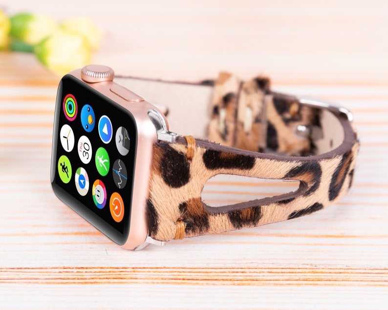 May include: A rose gold Apple Watch with a leopard print leather band. The watch face displays a variety of apps, including a clock, compass, and weather.