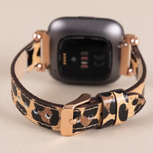 Puede incluir: Una correa de reloj de estampado de leopardo negro y dorado con una hebilla de oro rosa. La correa est&aacute; dise&ntilde;ada para un reloj inteligente con una cara cuadrada.
