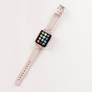 Pode incluir: Uma pulseira de rel&oacute;gio Apple de couro rosa claro com strass. O mostrador do rel&oacute;gio exibe uma variedade de aplicativos.
