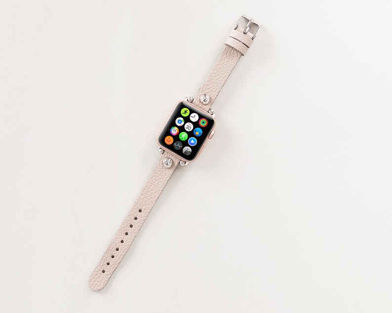 Pode incluir: Uma pulseira de rel&oacute;gio Apple de couro rosa claro com strass. O mostrador do rel&oacute;gio exibe uma variedade de aplicativos.