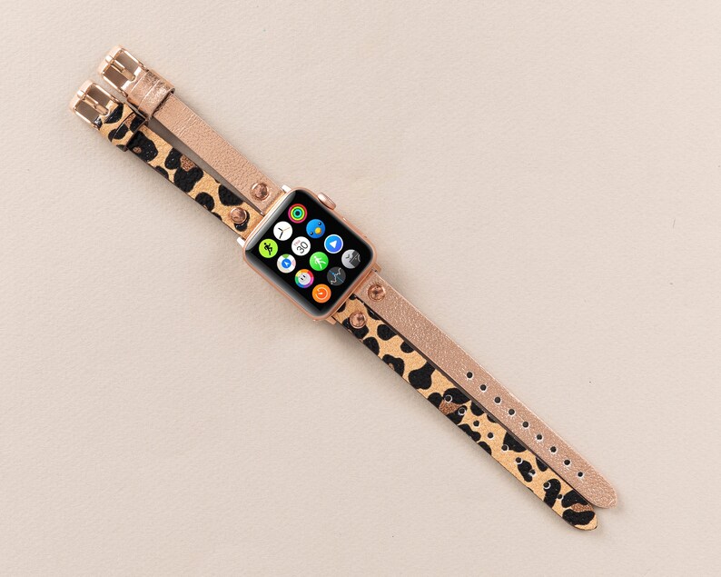 Może przedstawiać: Złoty pasek do Apple Watch z nadrukiem lamparta o podw&oacute;jnym pasku. Tarcza zegarka jest widoczna i pokazuje r&oacute;żne aplikacje.