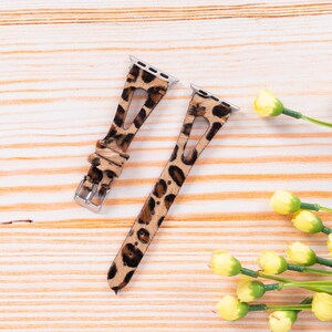 May include: Two leopard print watch bands for an Apple Watch. The bands are brown and black with a leopard print pattern. The bands are made of leather and have a metal buckle.