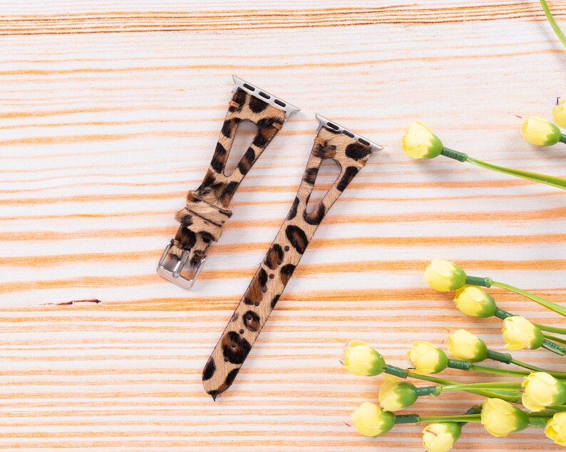 May include: Two leopard print watch bands for an Apple Watch. The bands are brown and black with a leopard print pattern. The bands are made of leather and have a metal buckle.