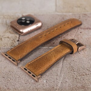 May include: Two brown leather watch straps with gold metal clasps and connectors. The straps are made of a textured leather and have a distressed look.