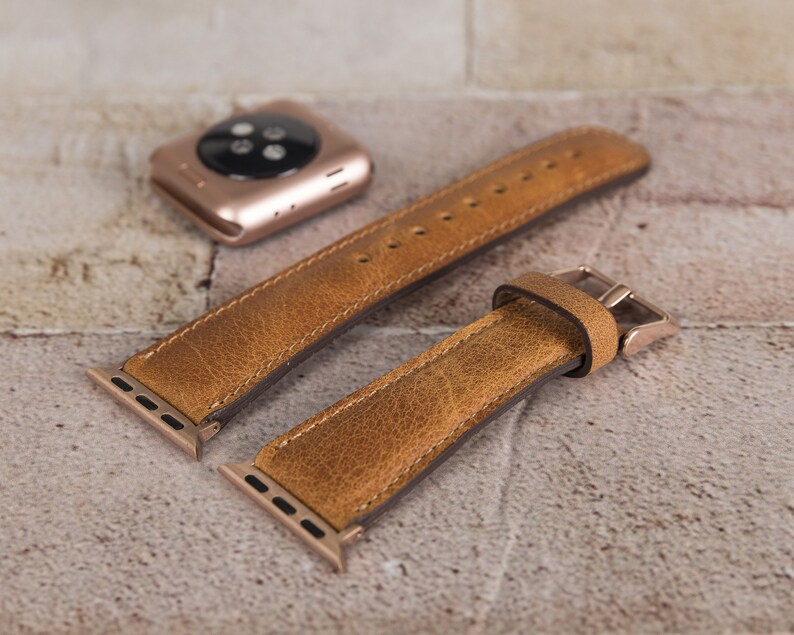 May include: Two brown leather watch straps with gold metal clasps and connectors. The straps are made of a textured leather and have a distressed look.