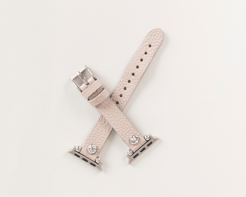 Pode incluir: Uma pulseira de rel&oacute;gio de couro bege claro com detalhes prateados e strass transparentes. A pulseira &eacute; projetada para um Apple Watch.