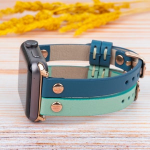 May include: A teal and light green leather Apple Watch band with gold accents and a buckle closure.