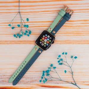 May include: A two-toned watch band in teal and light green with gold accents. The band is made of leather and has a buckle closure.