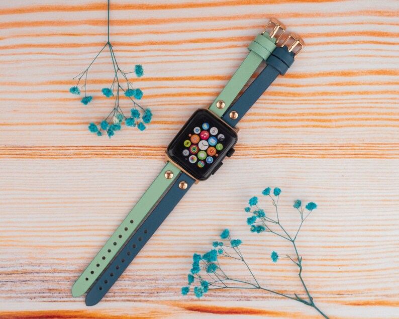 May include: A two-toned watch band in teal and light green with gold accents. The band is made of leather and has a buckle closure.
