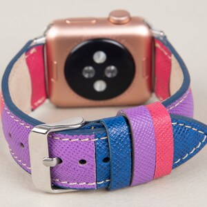Puede incluir: Una correa de reloj de cuero colorida con rayas moradas, rosas y azules. La correa est&aacute; dise&ntilde;ada para un Apple Watch y tiene una hebilla plateada.