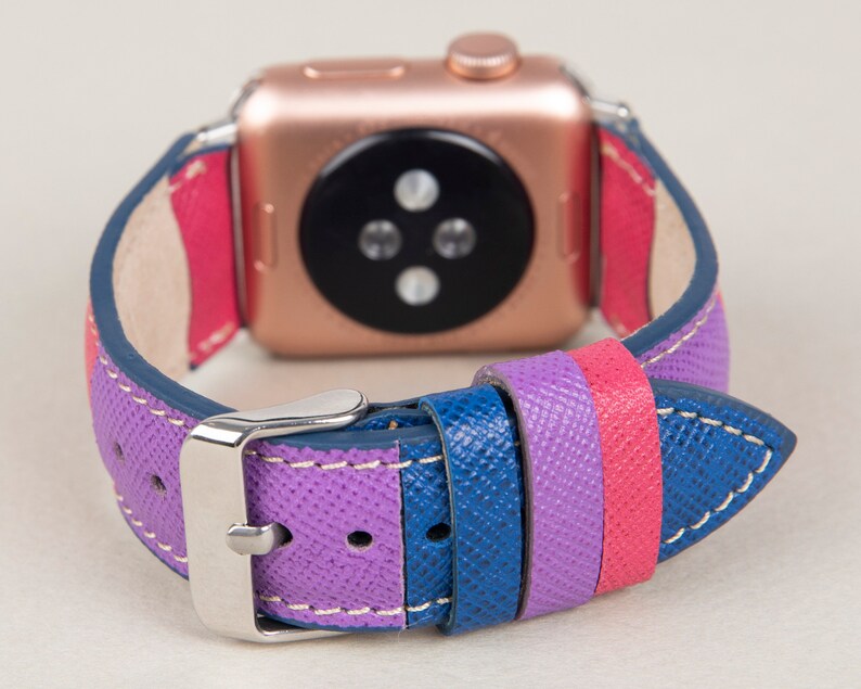 Puede incluir: Una correa de reloj de cuero colorida con rayas moradas, rosas y azules. La correa est&aacute; dise&ntilde;ada para un Apple Watch y tiene una hebilla plateada.