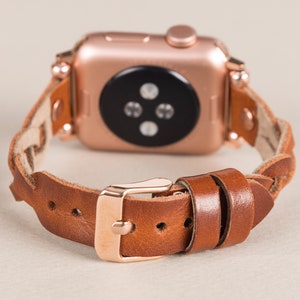 Puede incluir: Una correa de reloj trenzada de cuero marr&oacute;n con una hebilla de oro rosa y un Apple Watch de oro rosa.
