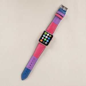 Puede incluir: Una banda de reloj Apple de cuero rosa, morado y azul con una esfera de reloj Apple dorada.