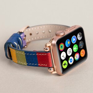K&ouml;nnte beinhalten: Eine ros&eacute;goldene Apple Watch mit einem bunten Lederarmband. Das Zifferblatt der Uhr zeigt verschiedene App-Symbole an, darunter eine Uhr, einen Herzfrequenzmesser und einen Kompass.