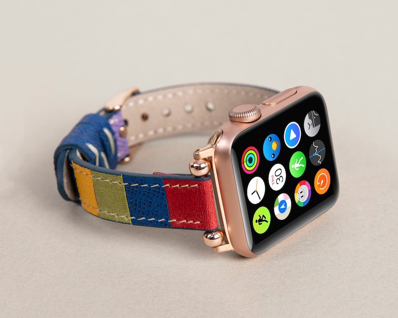 K&ouml;nnte beinhalten: Eine ros&eacute;goldene Apple Watch mit einem bunten Lederarmband. Das Zifferblatt der Uhr zeigt verschiedene App-Symbole an, darunter eine Uhr, einen Herzfrequenzmesser und einen Kompass.