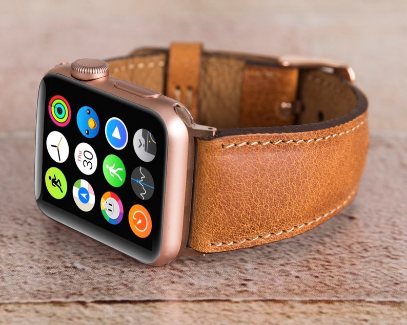 May include: A rose gold Apple Watch with a brown leather strap. The watch face shows a variety of app icons.