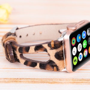 May include: A rose gold Apple Watch with a leopard print band. The watch face is black with a variety of colorful app icons.