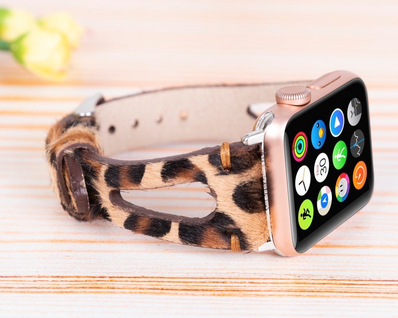 May include: A rose gold Apple Watch with a leopard print band. The watch face is black with a variety of colorful app icons.