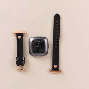 May include: A black leather watch band with rose gold hardware and a gray fitness tracker with a black screen.