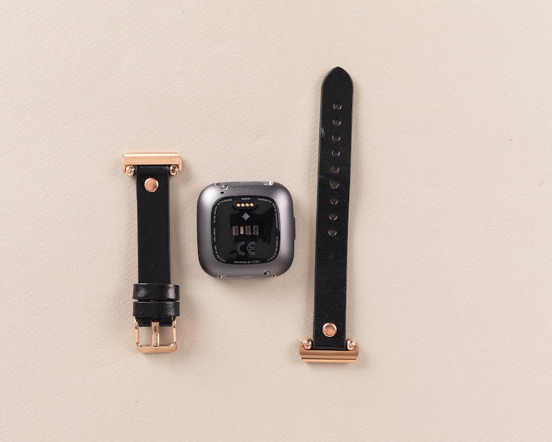 May include: A black leather watch band with rose gold hardware and a gray fitness tracker with a black screen.