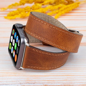 K&ouml;nnte beinhalten: Ein braunes Lederarmband f&uuml;r die Apple Watch mit gen&auml;htem Rand. Das Armband ist um eine silberne Apple Watch mit schwarzem Zifferblatt gewickelt.