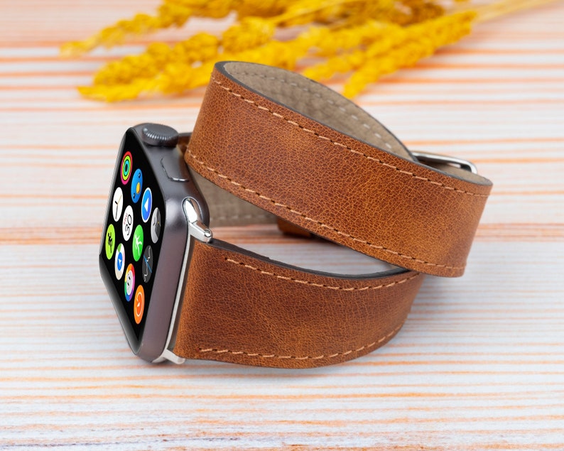K&ouml;nnte beinhalten: Ein braunes Lederarmband f&uuml;r die Apple Watch mit gen&auml;htem Rand. Das Armband ist um eine silberne Apple Watch mit schwarzem Zifferblatt gewickelt.