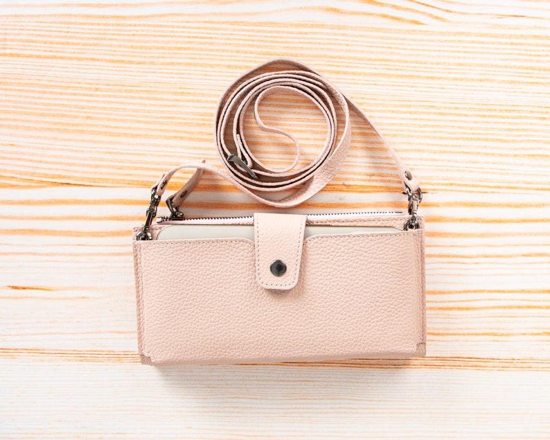 Pu&ograve; includere: Un portafoglio a tracolla color rosa pallido con texture granulata di forma rettangolare, dotato di chiusura centrale con bottone a pressione, scomparto superiore con cerniera e tracolla regolabile abbinata con attacchi in metallo argentato.