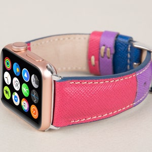 Puede incluir: Un Apple Watch de oro rosa con una banda de cuero rosa, morado y azul. La esfera del reloj muestra varios iconos de aplicaciones.