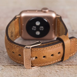 May include: A brown leather watch strap with a rose gold buckle and a rose gold Apple Watch face.