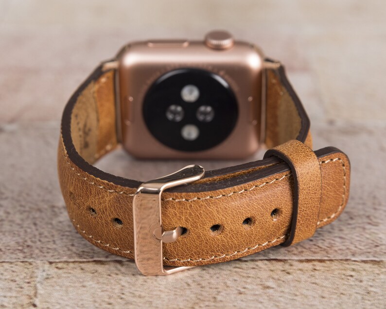 May include: A brown leather watch strap with a rose gold buckle and a rose gold Apple Watch face.