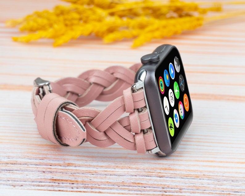 K&ouml;nnte beinhalten: Ein rosafarbenes geflochtenes Lederarmband f&uuml;r eine Apple Watch. Das Armband besteht aus geflochtenen Lederriemen und hat eine silberne Schnalle.