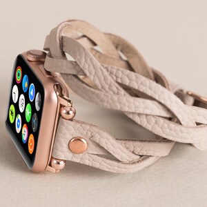 Op de afbeelding: Een Apple Watch in ros&eacute; goud met een wit gevlochten leren bandje. Het horloge-scherm toont verschillende apps.