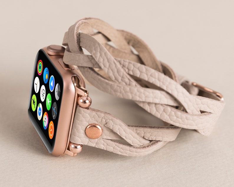 Op de afbeelding: Een Apple Watch in ros&eacute; goud met een wit gevlochten leren bandje. Het horloge-scherm toont verschillende apps.